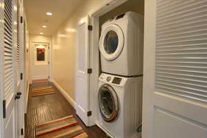 Laundry room with stacked washer and clothes dryer, recessed lighting, and dark wood-style flooring