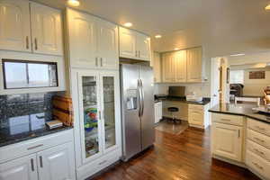 Kitchen featuring stainless steel fridge with ice dispenser, white cabinetry, dark wood-type flooring, recessed lighting, and dark stone countertops