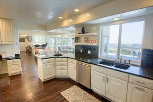 Kitchen with a peninsula, stainless steel dishwasher, dark wood-style floors, white cabinetry, and recessed lighting