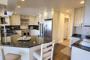 Kitchen with a peninsula, appliances with stainless steel finishes, wall chimney exhaust hood, recessed lighting, and dark wood-type flooring