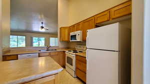 Kitchen featuring white appliances, light countertops, brown cabinetry, and a ceiling fan
