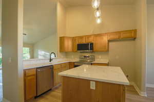 Kitchen with stainless steel appliances, light wood-style floors, light stone counters, wood finish cabinetry, and a high ceiling