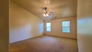 Carpeted empty room with a ceiling fan and vaulted ceiling