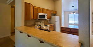 Kitchen with brown cabinetry, white appliances, light countertops, pendant lighting, and a kitchen breakfast bar