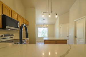 Kitchen with stainless steel range with electric stovetop, wood finish cabinetry, light stone counters, suspended lighting, and a center island