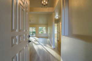 Hallway featuring light wood finished floors, a textured wall, and a chandelier