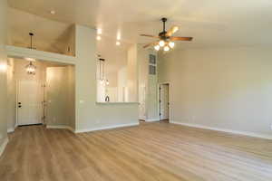 Unfurnished living room featuring light wood finished floors, lofted ceiling, ceiling fan, and hanging lights