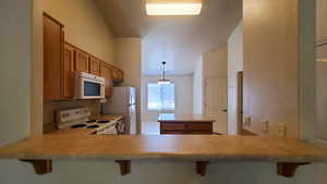 Kitchen with brown cabinetry, white appliances, a peninsula, light countertops, and a breakfast bar