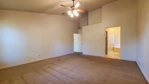 Unfurnished bedroom featuring a towering ceiling, carpet, ensuite bath, and ceiling fan