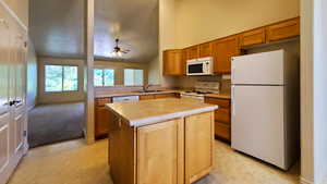 Kitchen with white appliances, a ceiling fan, a kitchen island, light countertops, and high vaulted ceiling