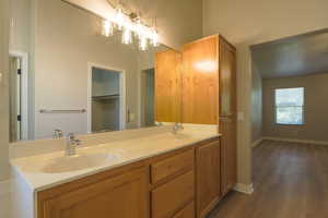 Full bath with double vanity, dark wood finished floors, and a walk in closet