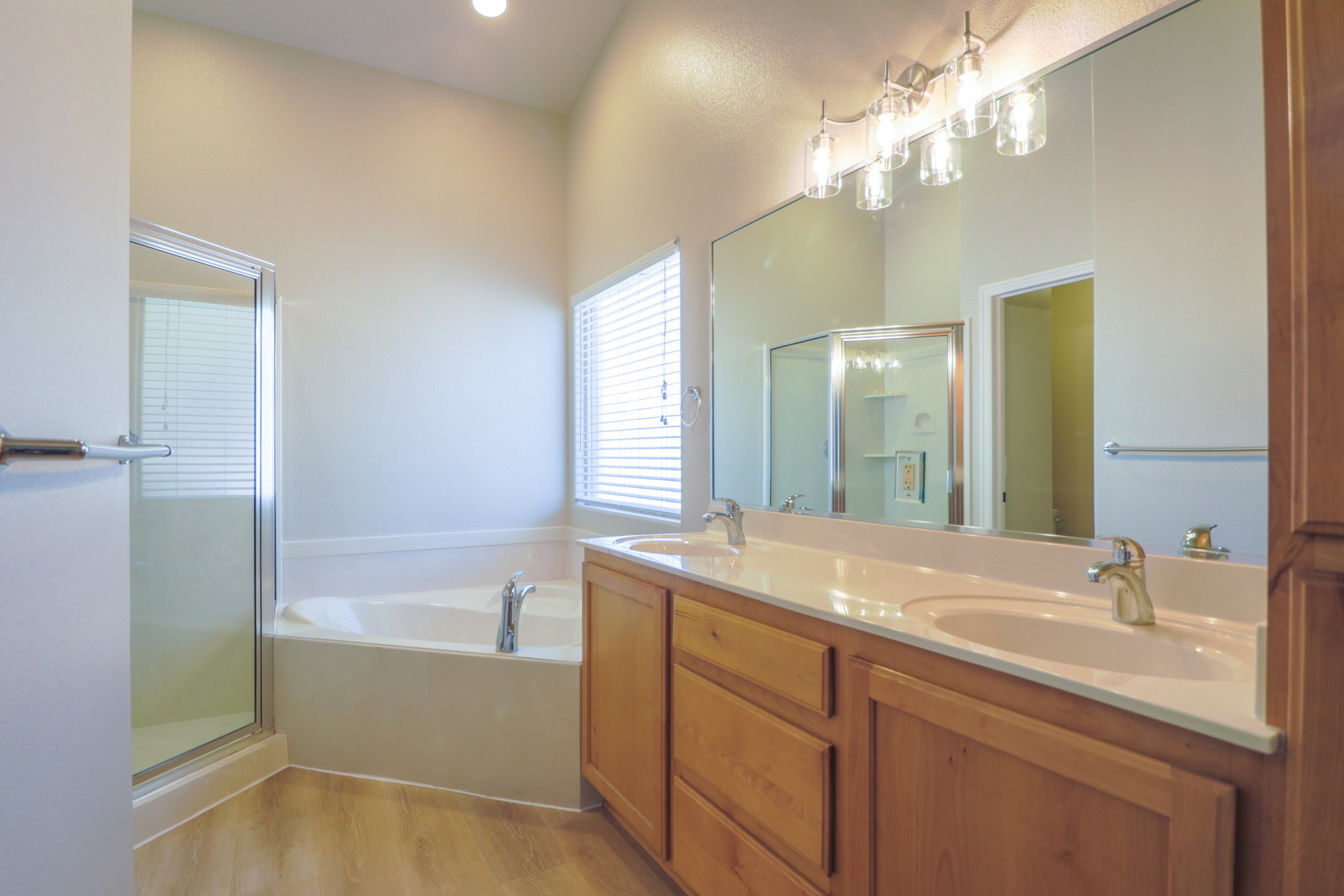 Full bath with double vanity, a stall shower, a bath, and light wood-style flooring