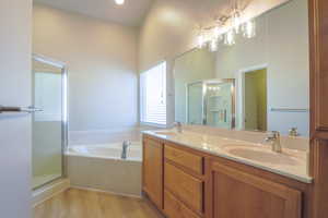 Full bath with double vanity, a stall shower, a bath, and light wood-style flooring