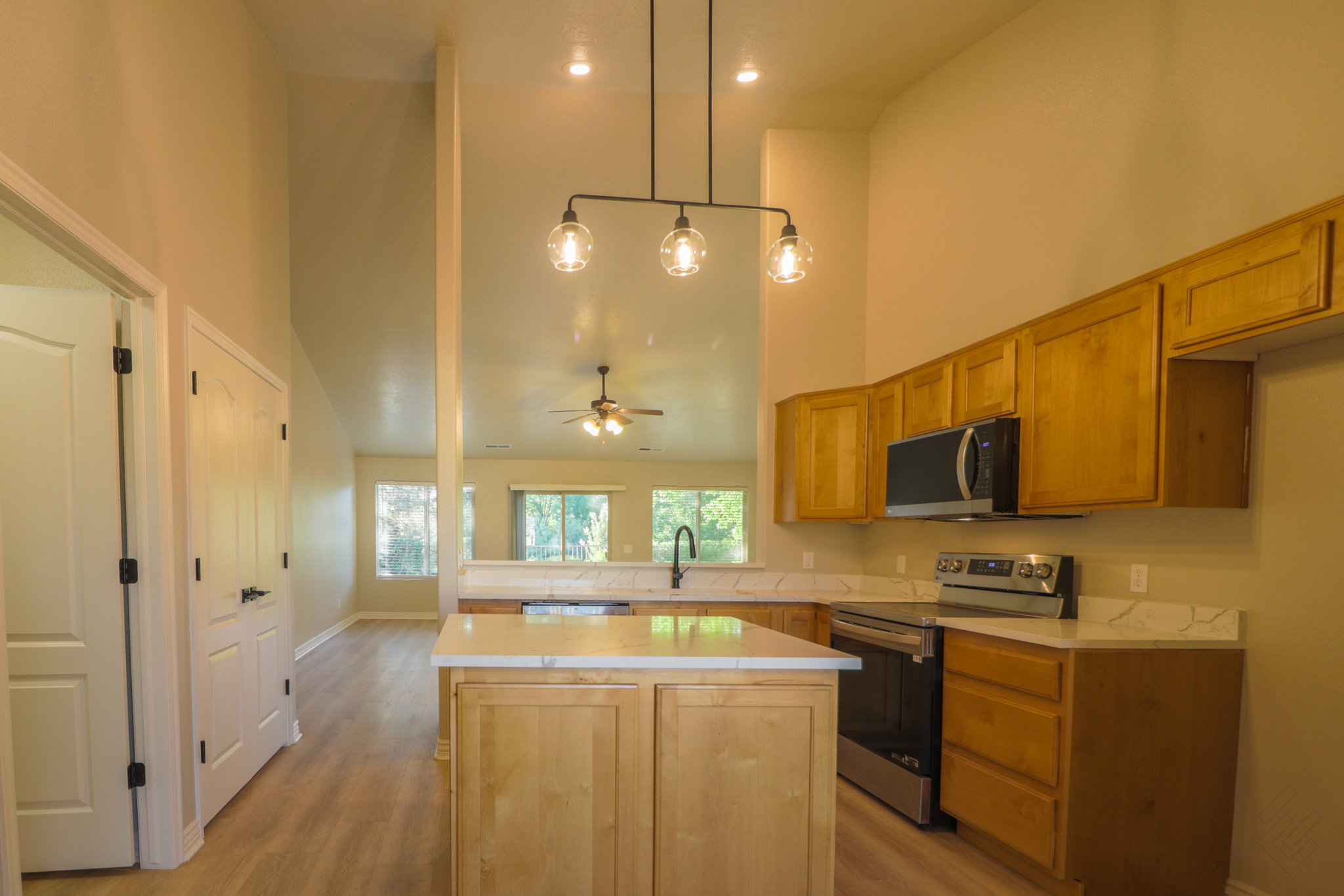 Kitchen featuring stainless steel appliances, a center island, a high ceiling, light wood-style flooring, and a ceiling fan