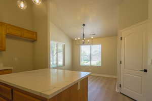 Kitchen with a center island, lofted ceiling, light wood-style flooring, a chandelier, and wood finish cabinetry