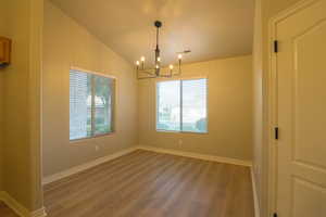 Unfurnished room featuring dark wood-type flooring, hanging lights, and vaulted ceiling