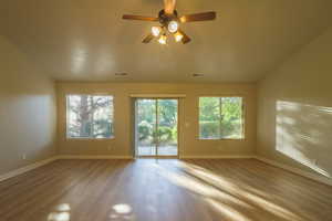 Spare room featuring dark wood-style floors, plenty of natural light, a ceiling fan, and lofted ceiling