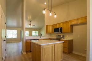 Kitchen featuring stainless steel appliances, dark wood-style floors, ceiling fan, a kitchen island, and vaulted ceiling