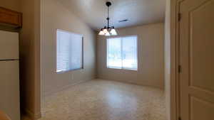 Empty room with a chandelier, light floors, and vaulted ceiling