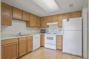 Kitchen featuring white appliances, light countertops, light wood-style flooring, and under cabinet range hood
