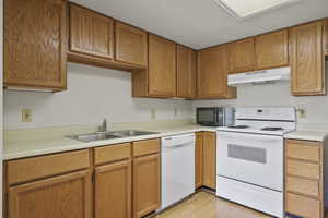 Kitchen with white appliances, light countertops, under cabinet range hood, light wood-type flooring, and brown cabinetry