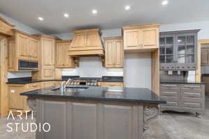 Kitchen featuring custom exhaust hood, recessed lighting, a kitchen island with sink, stainless steel microwave, and dark stone counters