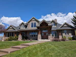 Craftsman-style home with a front yard, a porch, stone siding, a chimney, and roof with shingles