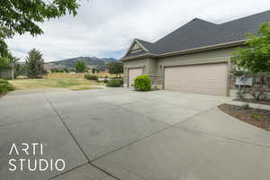 View of side of property featuring a mountain view, concrete driveway, a shingled roof, a garage, and stone siding