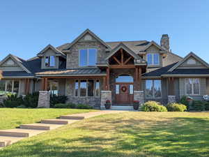 Craftsman-style home featuring roof with shingles, stone siding, a front yard, and a chimney