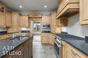Kitchen featuring stainless steel appliances, custom range hood, recessed lighting, dark stone counters, and light brown cabinetry
