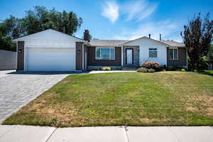 Ranch-style home with decorative driveway, an attached garage, a chimney, a front yard, and brick siding