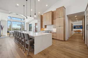 Kitchen with modern cabinets, high vaulted ceiling, a large island with sink, a breakfast bar area, and light wood-type flooring