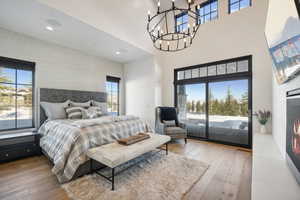 Bedroom featuring access to exterior, hardwood / wood-style flooring, multiple windows, a towering ceiling, and a chandelier