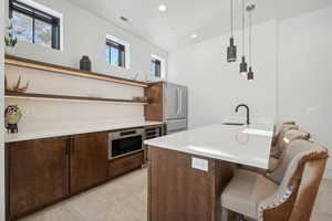 Kitchen featuring open shelves, a breakfast bar, dark brown cabinetry, decorative light fixtures, and light countertops