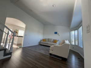 Living area with arched walkways, stairway, dark wood finished floors, a textured ceiling, and high vaulted ceiling