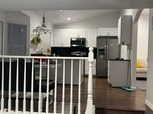 Kitchen with vaulted ceiling, stainless steel appliances, dark wood finished floors, arched walkways, and white cabinets