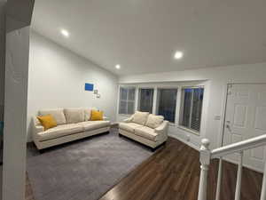 Living area with dark wood-style flooring, recessed lighting, and vaulted ceiling