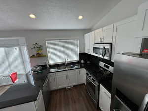 Kitchen with appliances with stainless steel finishes, dark countertops, a textured ceiling, dark wood finished floors, and white cabinets