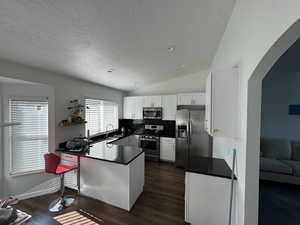 Kitchen with dark countertops, a peninsula, appliances with stainless steel finishes, arched walkways, and a textured ceiling
