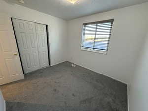 Unfurnished bedroom with a closet, dark carpet, and a textured ceiling