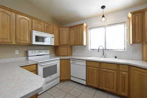 Kitchen featuring white appliances, backsplash, light tile patterned floors, light countertops, and vaulted ceiling