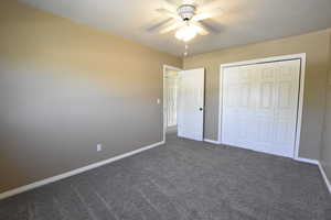 Unfurnished bedroom featuring dark carpet, a closet, and ceiling fan