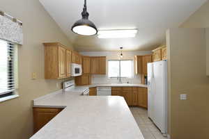 Kitchen featuring white appliances, light countertops, backsplash, light tile patterned floors, and pendant lighting