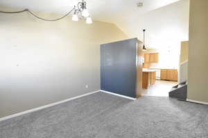 Unfurnished room featuring vaulted ceiling, light colored carpet, stairway, and a chandelier