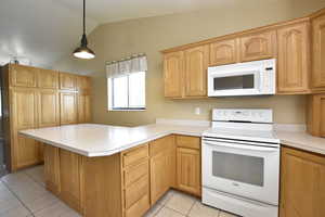 Kitchen featuring white appliances, a peninsula, vaulted ceiling, light tile patterned flooring, and light countertops