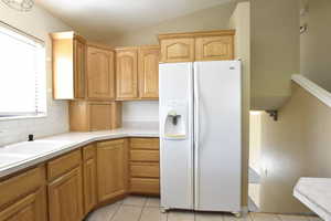 Kitchen with white fridge with ice dispenser, vaulted ceiling, light tile patterned flooring, light countertops, and tasteful backsplash