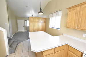 Kitchen with a peninsula, light brown cabinetry, lofted ceiling, light countertops, and light tile patterned floors