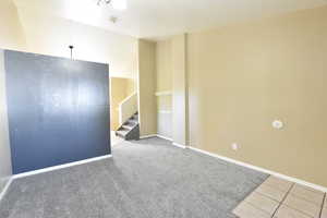 Carpeted empty room with stairway and tile patterned floors