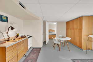 Kitchen with white range with gas stovetop, a drop ceiling, finished concrete floors, and light countertops