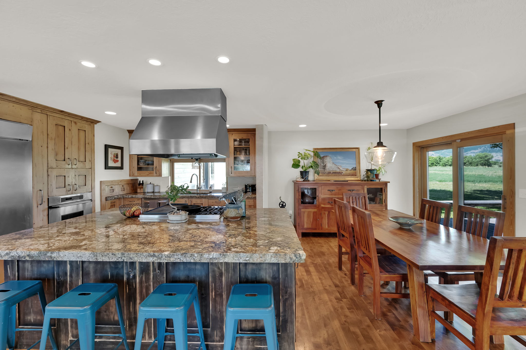 Kitchen featuring wall chimney exhaust hood, recessed lighting, wood finished floors, glass insert cabinets, and appliances with stainless steel finishes